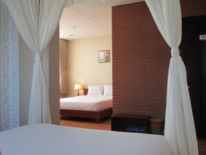 Habitación de hotel con una cama, una mesita de noche con lámpara, una pequeña mesa y una puerta con el número.