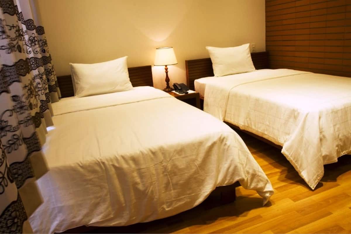 Two single beds with white linens, a bedside table with a lamp, and a wooden headboard.
