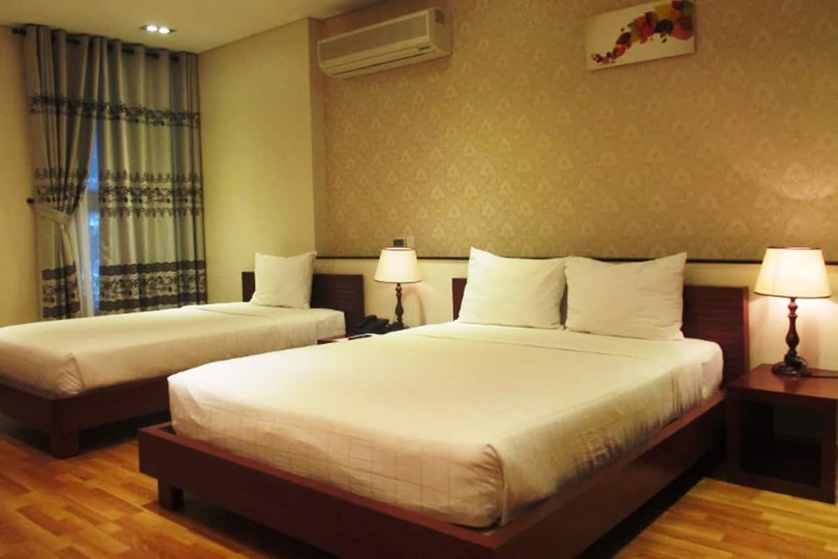 A hotel room with two beds, a wall-mounted air conditioner, and a decorative piece above the beds.