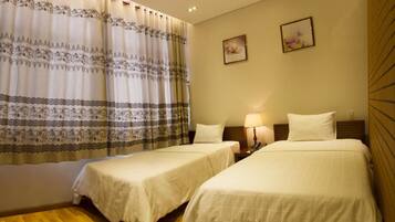 Habitación de hotel con dos camas individuales, una mesita de noche con lámpara y un ventanal con cortinas estampadas.