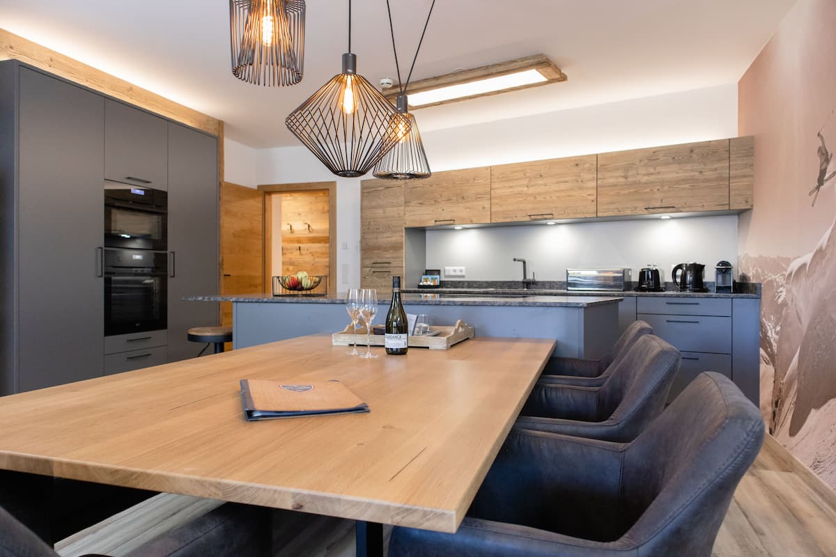 Una cocina moderna con una mesa de comedor de madera, taburetes de bar e iluminación colgante.