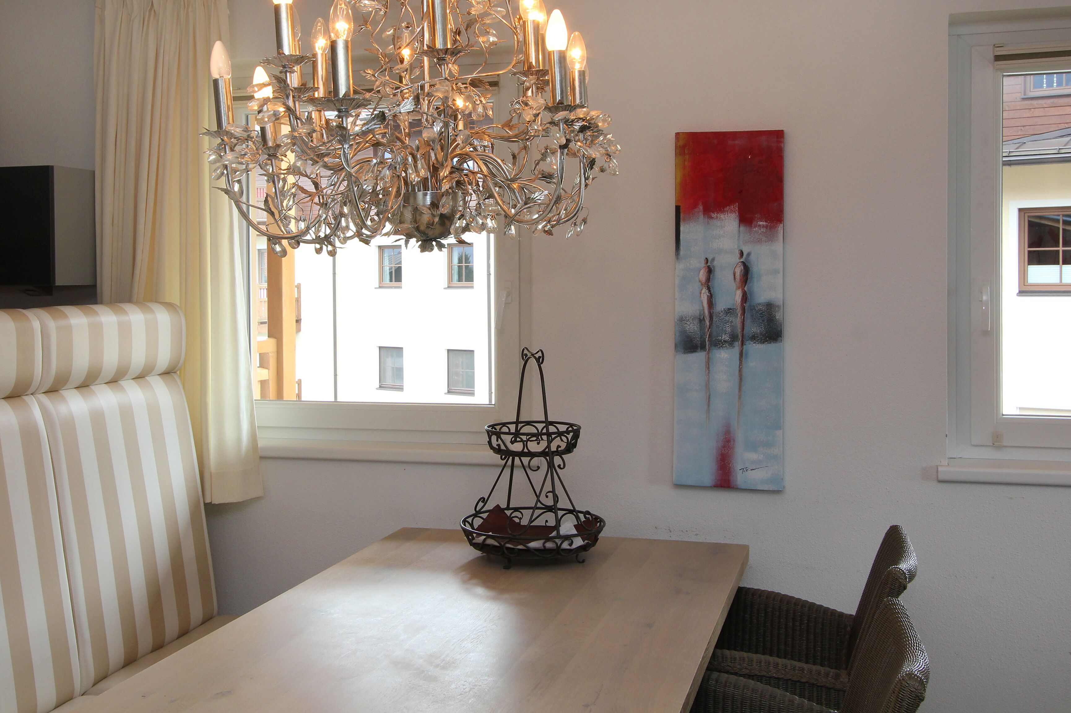 Ein Essbereich mit einer Chandelieber, einem Tisch, einer gepolsterten Bank und einem Gemälde an der Wand.