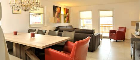 A modern living room with a dining area, a chandelier, and large windows.