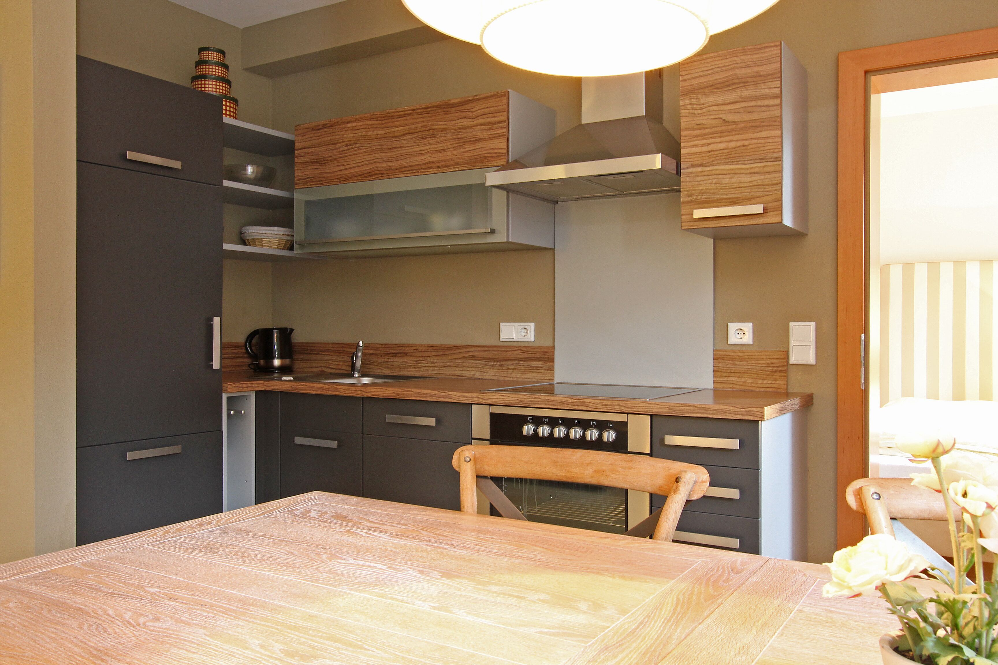Eine kompakte Küche mit einem Holztisch, Stühlen, einer Kaffeemaschine und einem eingebauten Backofen.