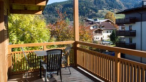 A wooden balcony with a table and chairs, overlooking a mountainous landscape with houses. - AvenidA Style Appartments by Alpin Rentals -incl Summercard (Kaprun)