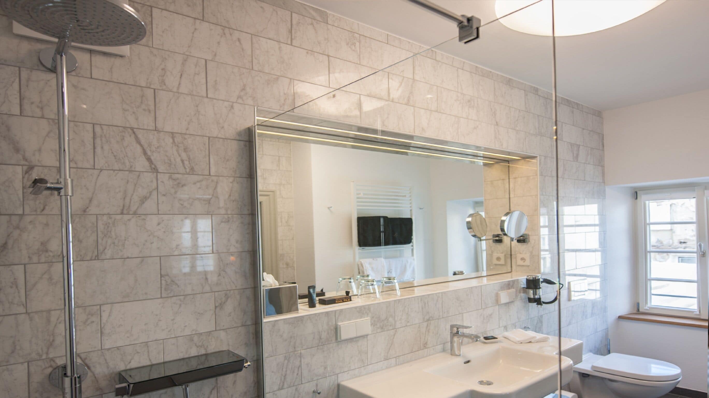 Un baño moderno con cabina de ducha de vidrio, un espejo grande, un lavabo blanco y un inodoro.