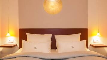 Quarto de hotel com uma cama de casal, duas mesas de cabeceira, luminária fixada na parede e um pequeno estante em cada mesa de apoio.