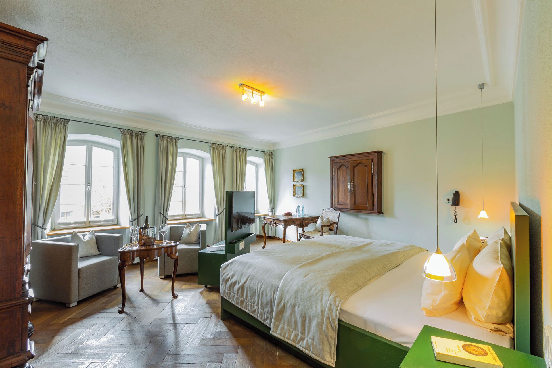 A hotel room with a bed, a sofa, a dining table, and a television.