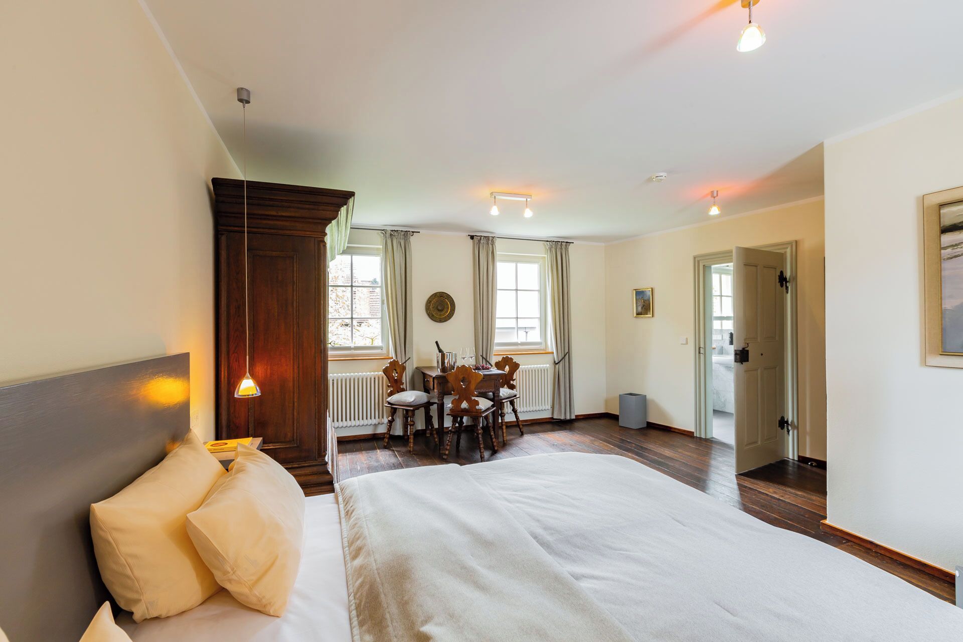 A bedroom with a large bed, a wooden headboard, a dining table with chairs, and a view of the outside through a window.