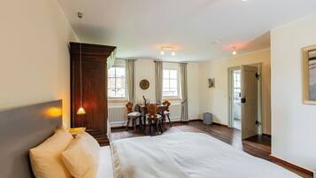 A bedroom with a large bed, a wooden headboard, a dining table with chairs, and a view of the outside through a window.