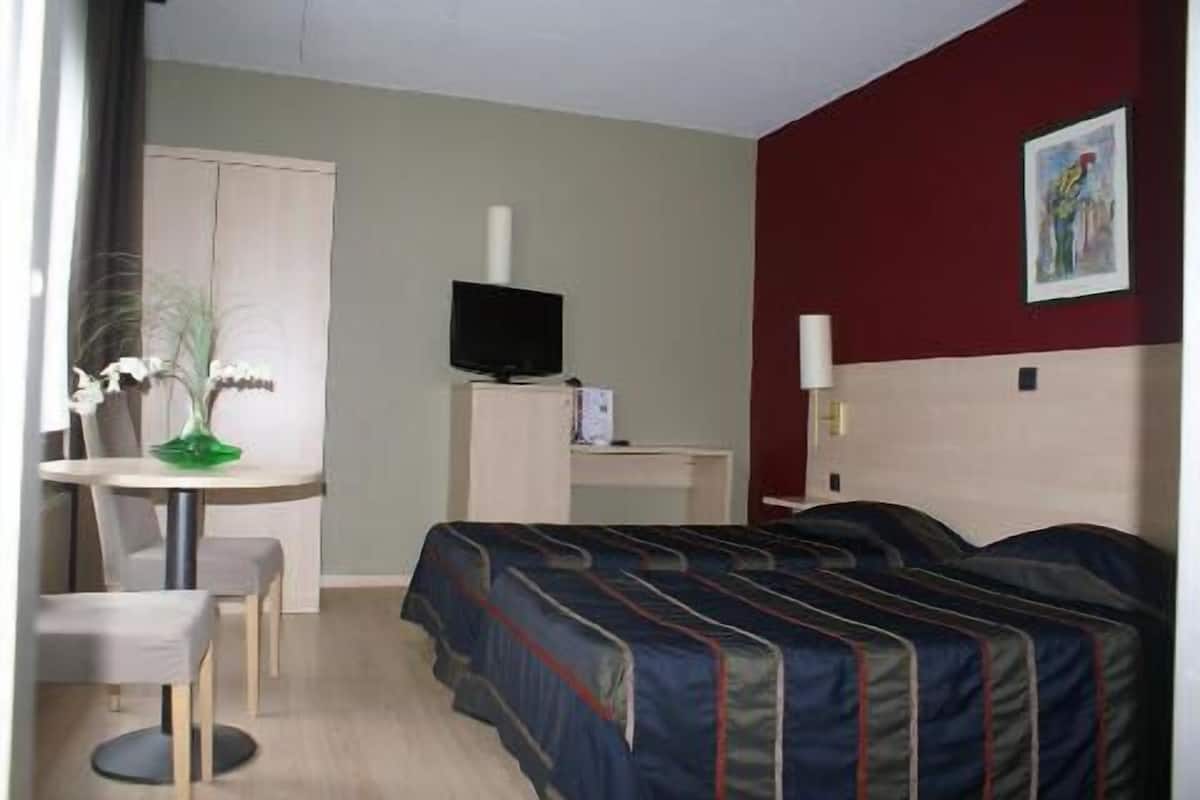 A hotel room with a bed, a desk, a chair, a television, and a painting on the wall.