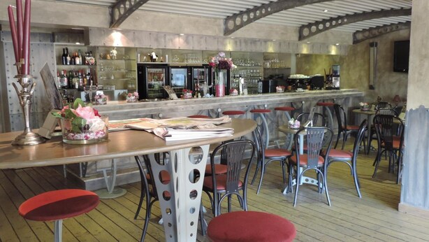 Zona de bar con taburetes, una barra y una variedad de botellas y vasos.