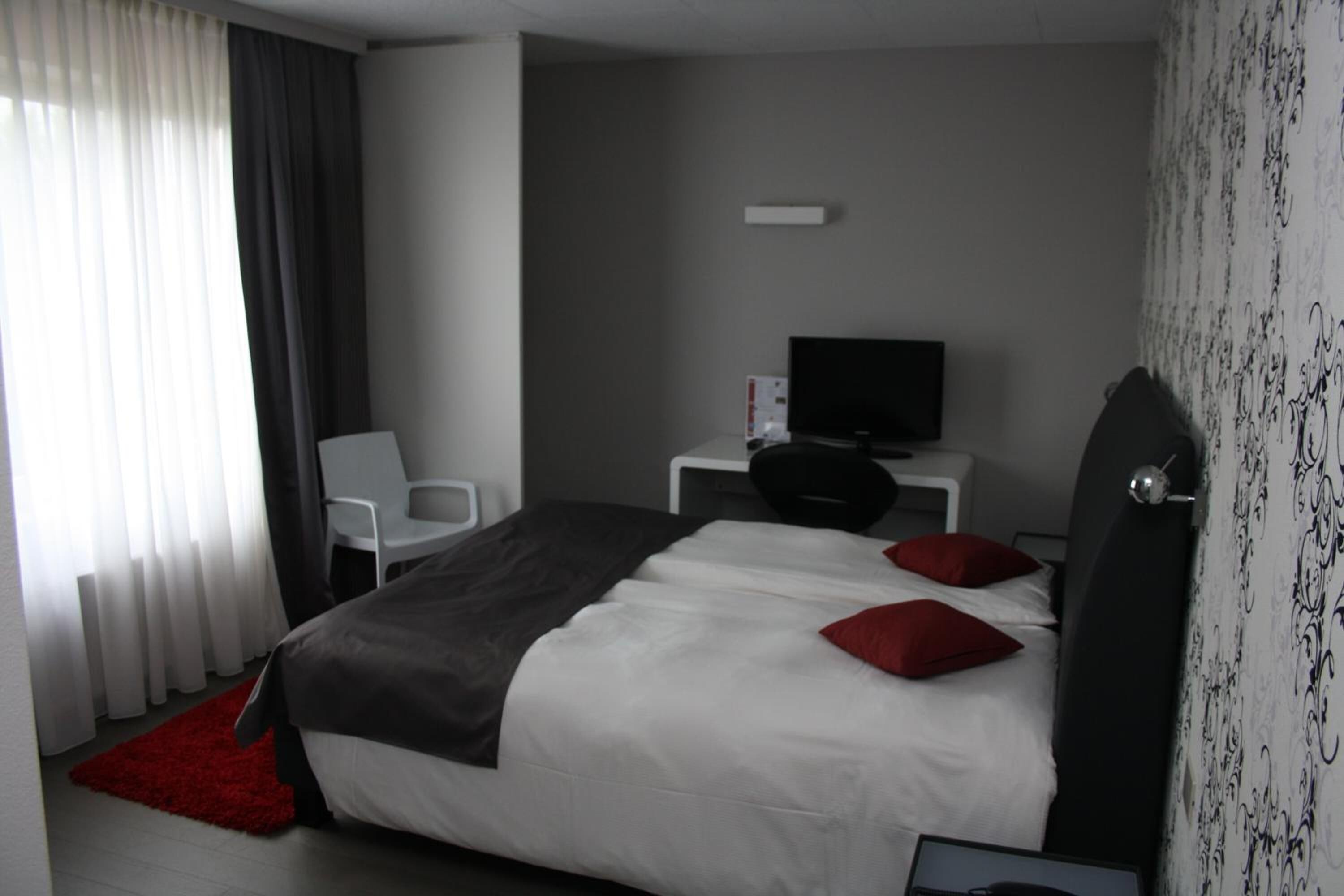 A hotel room with a large bed, a desk with a TV, a chair, and a red rug.