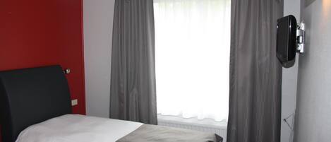 Une chambre d’hôtel avec un lit, un mur d’accent rouge, des rideaux gris et un téléviseur fixé au mur.