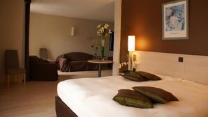 Habitación de hotel con una cama grande, una silla, una mesita con un florero y un cuadro en la pared.
