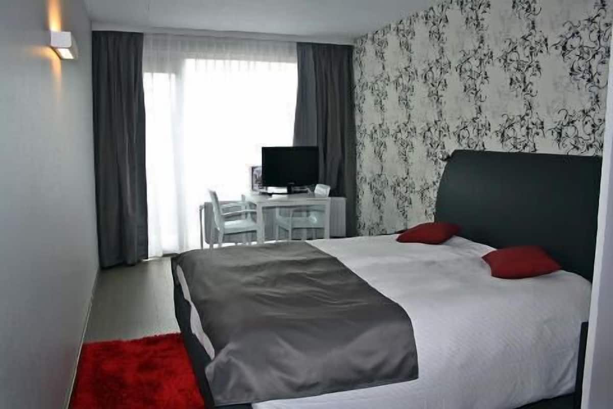 A hotel room with a bed, a desk with a computer, a chair, and a TV.