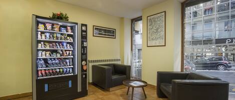 A lobby with a vending machine, seating area, and a window with a view of the street.