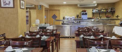 Un restaurante con mesas y sillas de madera, una zona de bar y una cocina al fondo.