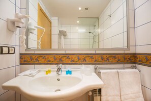 A bathroom with a sink, mirror, hairdryer, and shower.