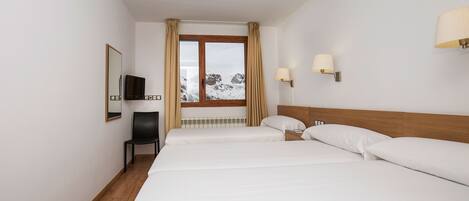 A hotel room with a wooden floor, a bed with white linens, a chair, a TV, and a window with curtains.