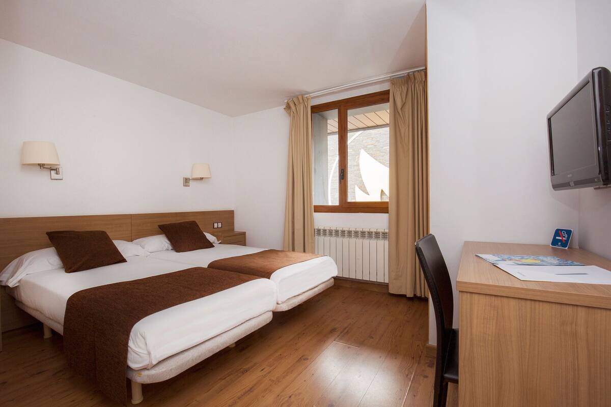 Habitación de hotel con dos camas, un escritorio, una silla, un televisor y una ventana con cortinas.