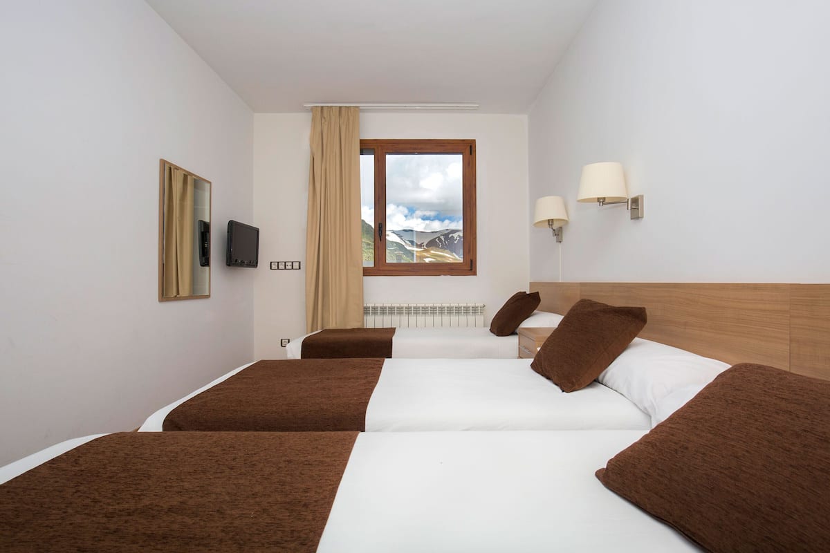 Habitación de hotel con dos camas, televisión, ventana y vista a la montaña, además de un calefactor.