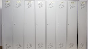 Een rij witte lockers genummerd van 202 tot 307, elk met een klein label en een eenvoudige tekening van ski’s.