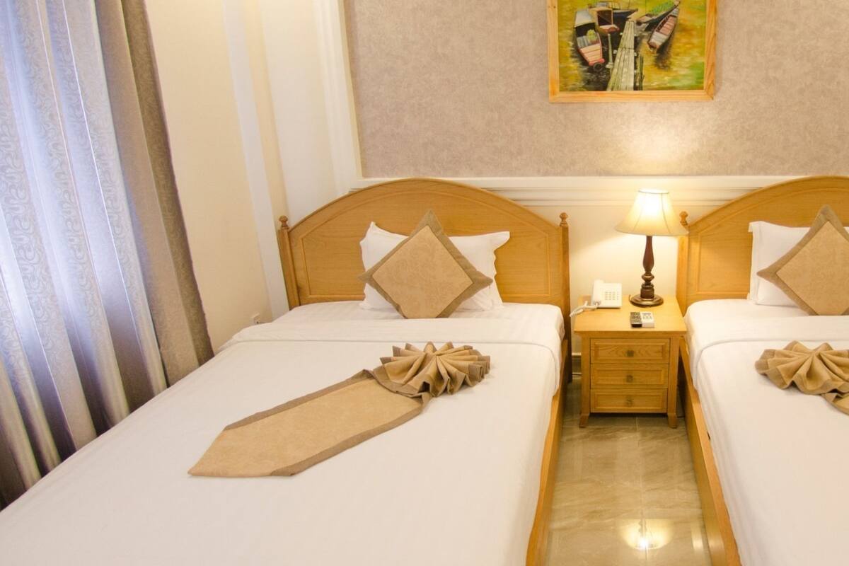 A hotel room with two beds, a nightstand with a lamp, and a painting on the wall.