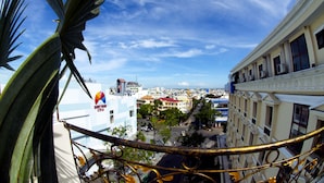 Vista desde un balcón con baranda de metal, sobre un paisaje urbano con edificios y cielo despejado.