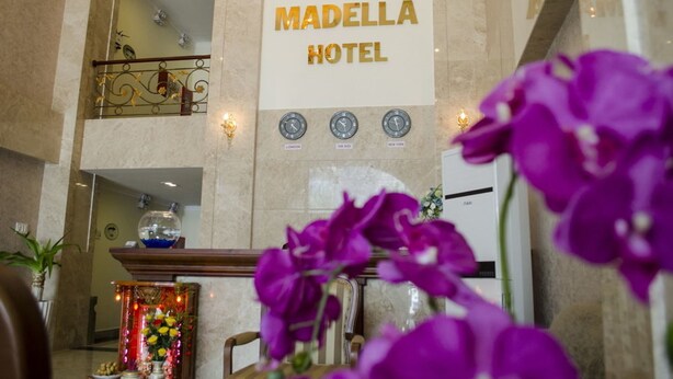 El interior del Hotel Madella, con una recepción, un reloj que marca la hora de Londres y una pared decorativa con un arreglo floral.