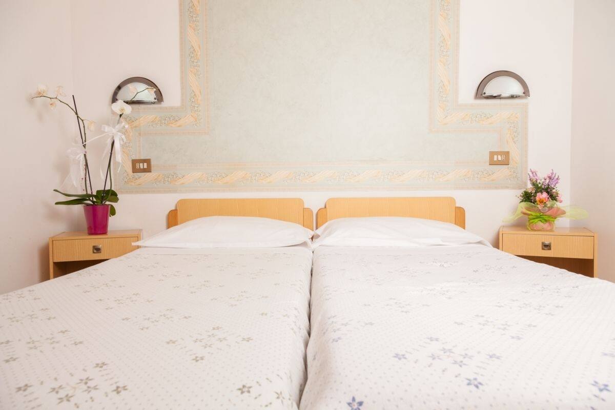 Un lit double avec une literie à motifs floraux, deux tables de chevet, un miroir et un mur orné d’un motif décoratif.