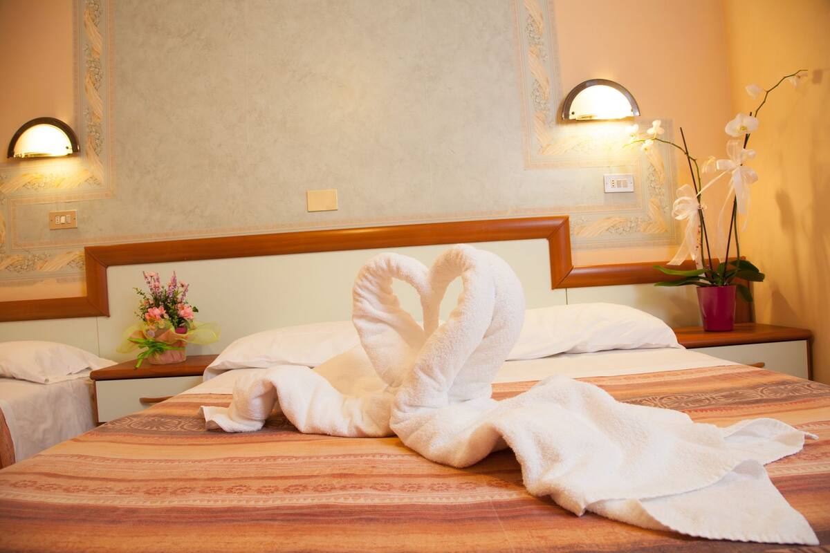 Une chambre d’hôtel avec un lit, deux tables de chevet, un arrangement floral et des appliques murales.