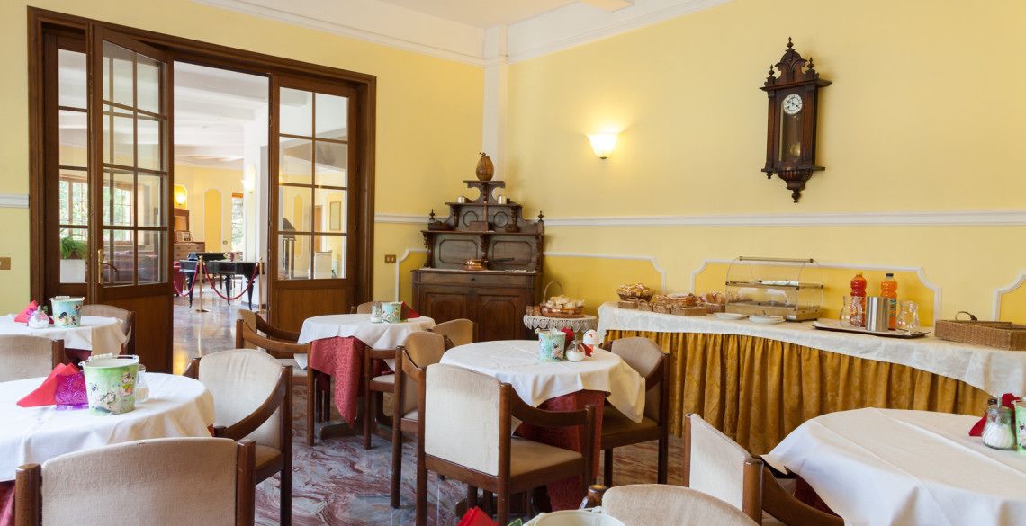Zona de dinar amb taules rodones, cadires, un aparador de menjar a granel i un rellotge antic a la paret.