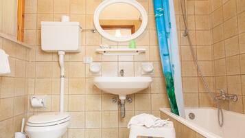 A bathroom with a toilet, sink, mirror, shower, and a small stool.