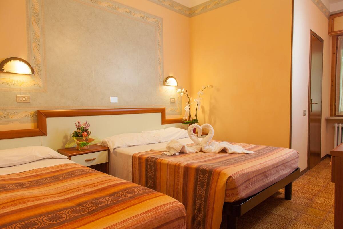 Une chambre d’hôtel avec deux lits, une table de chevet ornée d’un vase de fleurs et un mur agrémenté d’un panneau décoratif.