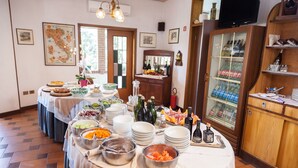 A buffet setup with various dishes and drinks, a television, and a wine rack in a room with tiled flooring and wooden furniture. - Hotel Residence Ricordo du Parc (Salsomaggiore Terme)