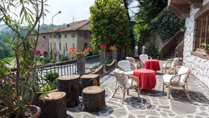 An outdoor patio with wicker chairs and tables, surrounded by potted plants and a stone wall. - Hotel Residence Ricordo du Parc (Salsomaggiore Terme)
