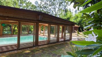 Una baita di legno con area piscina in vetro, immersa nel verde.