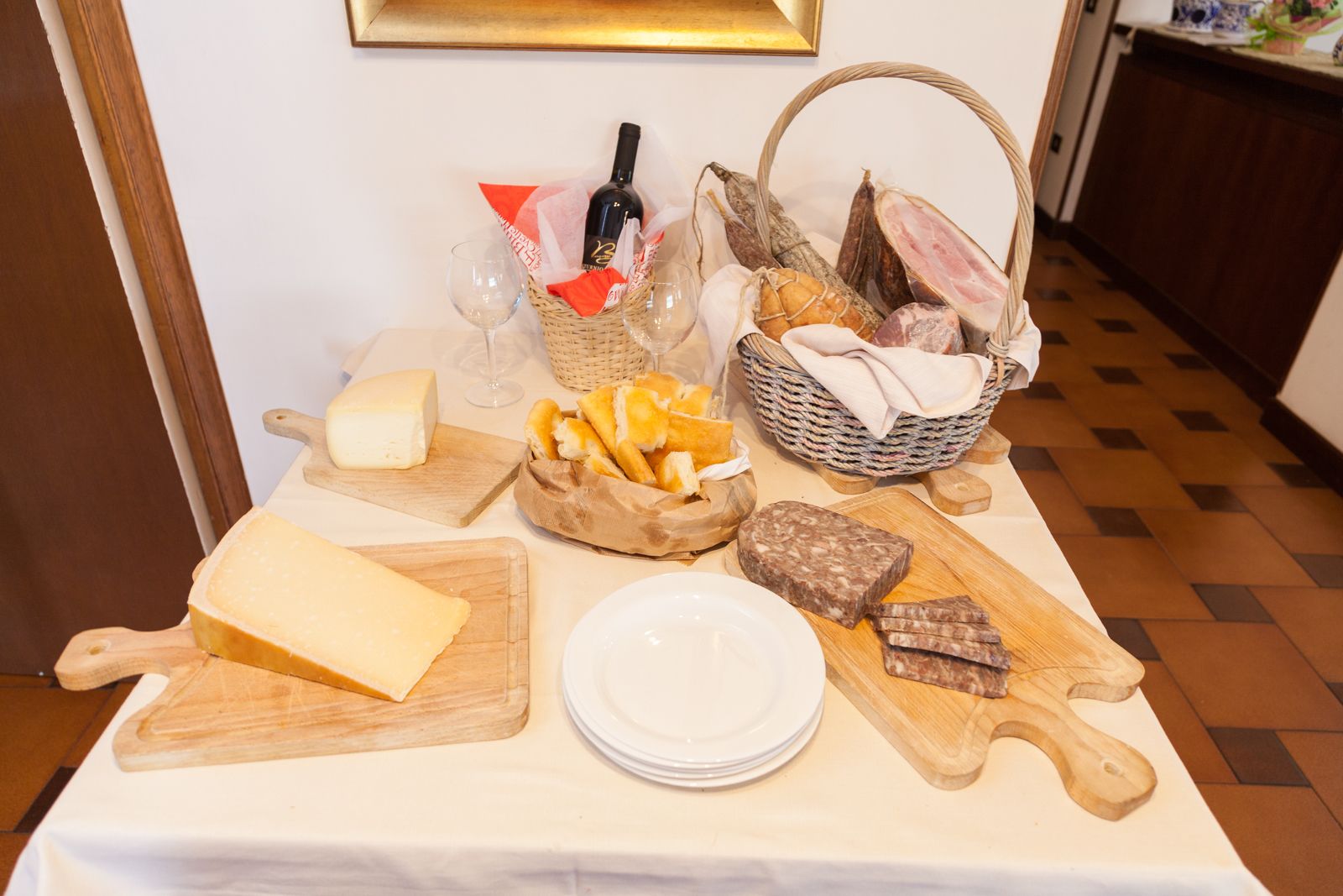 Una mesa con diversos alimentos, como queso, pan y embutidos, junto con una botella de vino y copas.