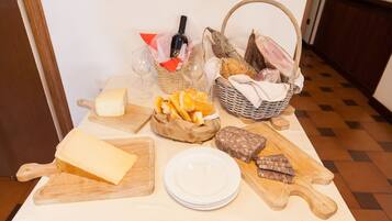 Una mesa con diversos alimentos, como queso, pan y embutidos, junto con una botella de vino y copas.