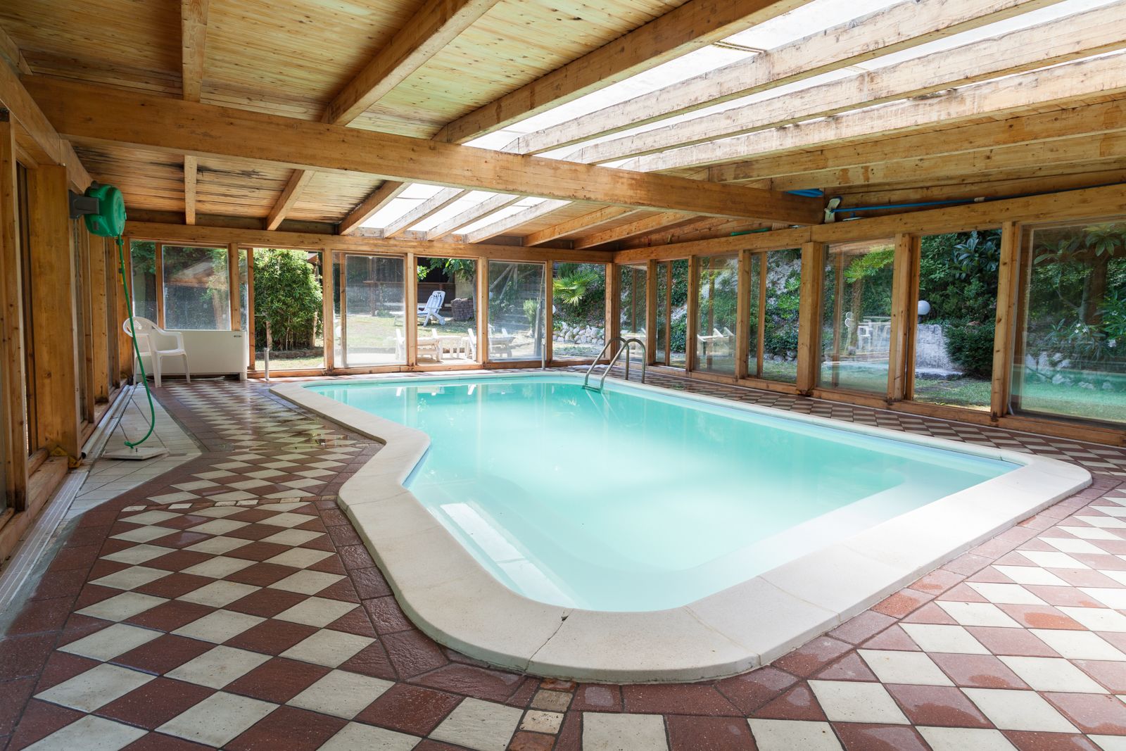 Una piscina interior con suelo a cuadros, vigas de madera y grandes ventanales.