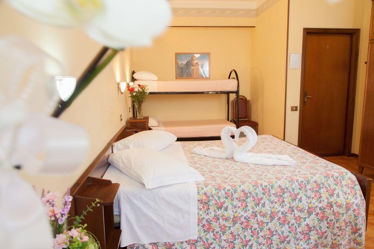 A hotel room with a bunk bed, a floral bedspread, a vase with flowers, and a painting on the wall.
