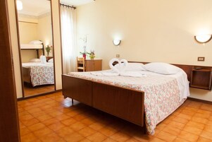 Una habitación de hotel con cama de madera, colcha estampada, espejo, mesita de noche y una lámpara de pared.