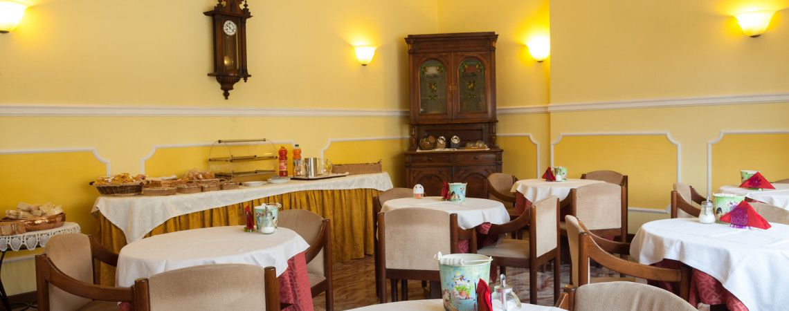 A dining area with tables set for service, a clock on the wall, and a cabinet with dishes.
