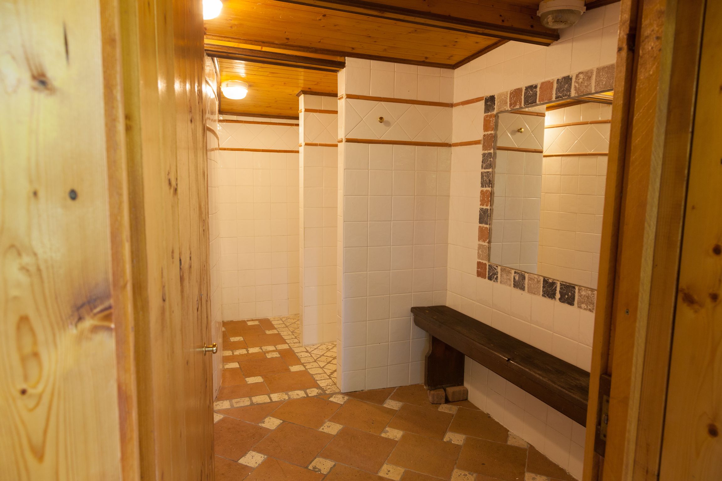 Un baño con paredes de azulejos blancos, un banco de madera y un piso de baldosas con diseño.