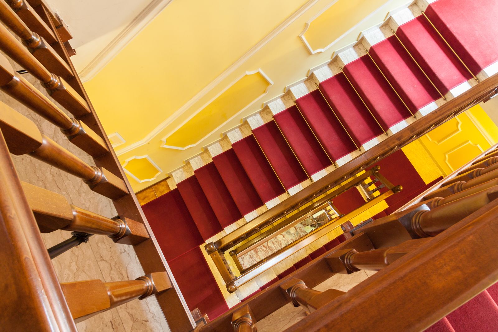 Un'imponente scalinata con una combinazione di colori rosso e giallo, che conduce a una zona con balcone e ringhiera in legno.