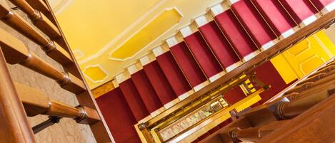 A grand staircase with a red and yellow color scheme, leading to a balcony area with a wooden railing.