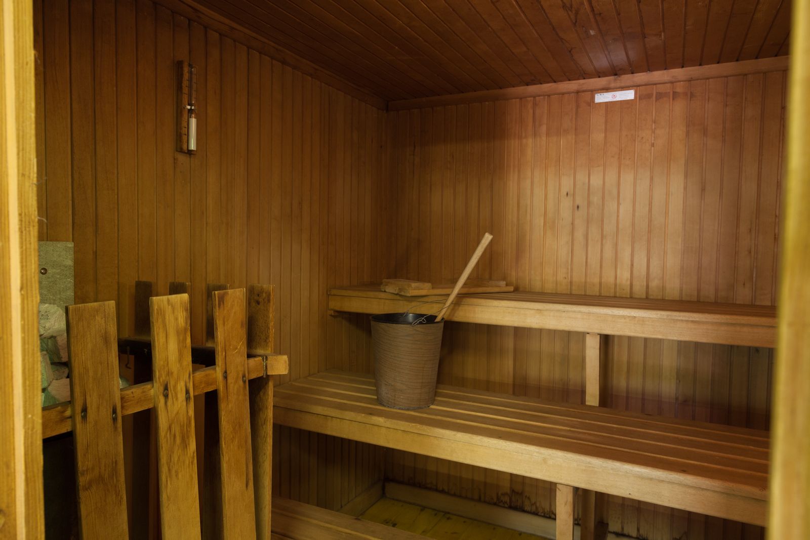 A wooden sauna with benches and a trash bin.
