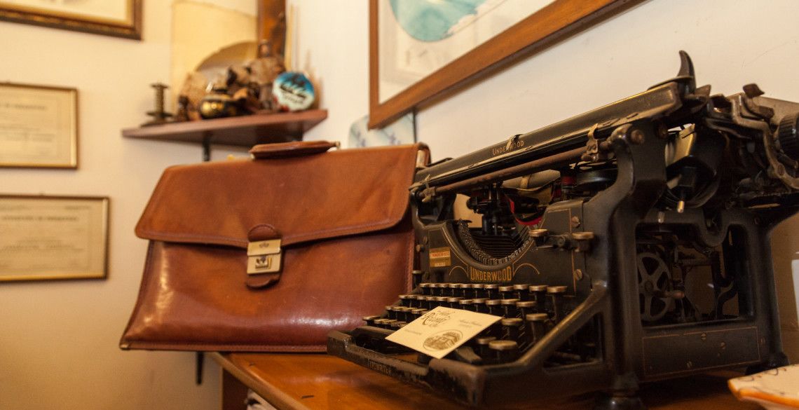 Eine antike Underwood Schreibmaschine auf einem Holztisch, neben ihr ein braunes Lederbriefcase.