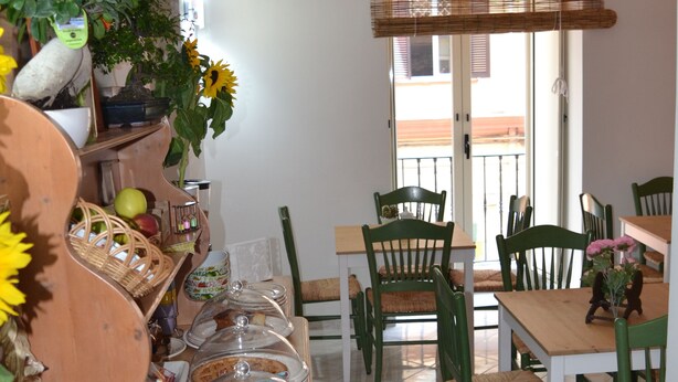 A dining area with wooden tables and chairs, a buffet setup with various food items, and a large window with a view of the outside. - Anna's Family (Naples)